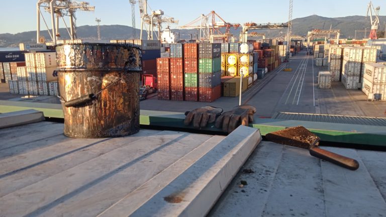 Imagen general del puerto de Vigo. En primer plano las herramientas de impermeabilización como guantes, cubo o espátula.