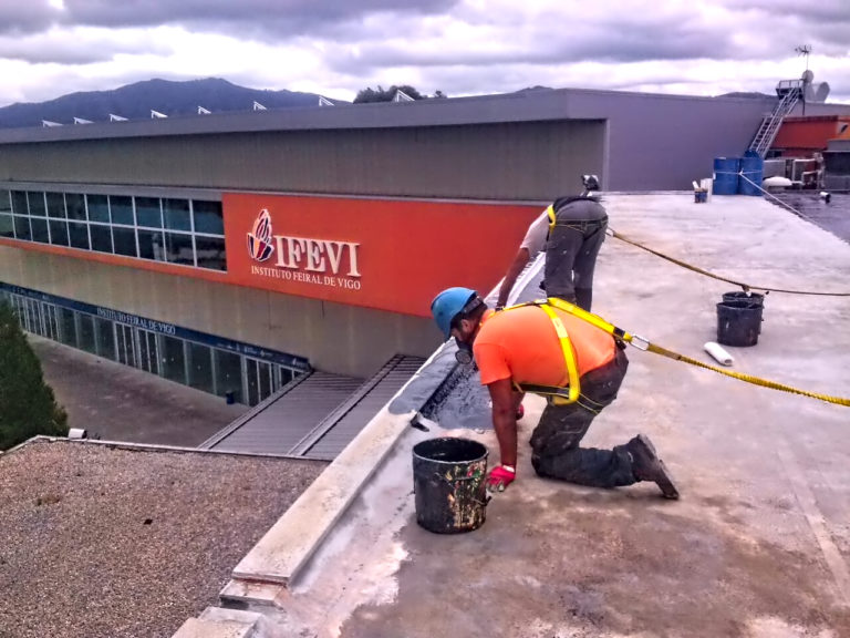 Imágenes de las obras de impermeabilización en el IFEVI. En la foto se ven dos obreros aplicando la impermeabilización en un tejado.